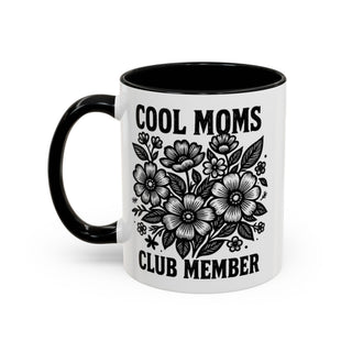 White mug with black rim, featuring a floral design and text "COOL MOMS CLUB MEMBER".