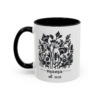 White mug with black handle and interior, featuring floral design and "mama est. 2026".