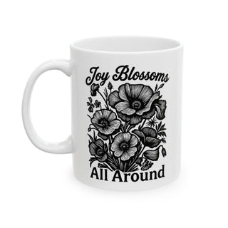 White mug with "Joy Blossoms All Around" text and a floral illustration.